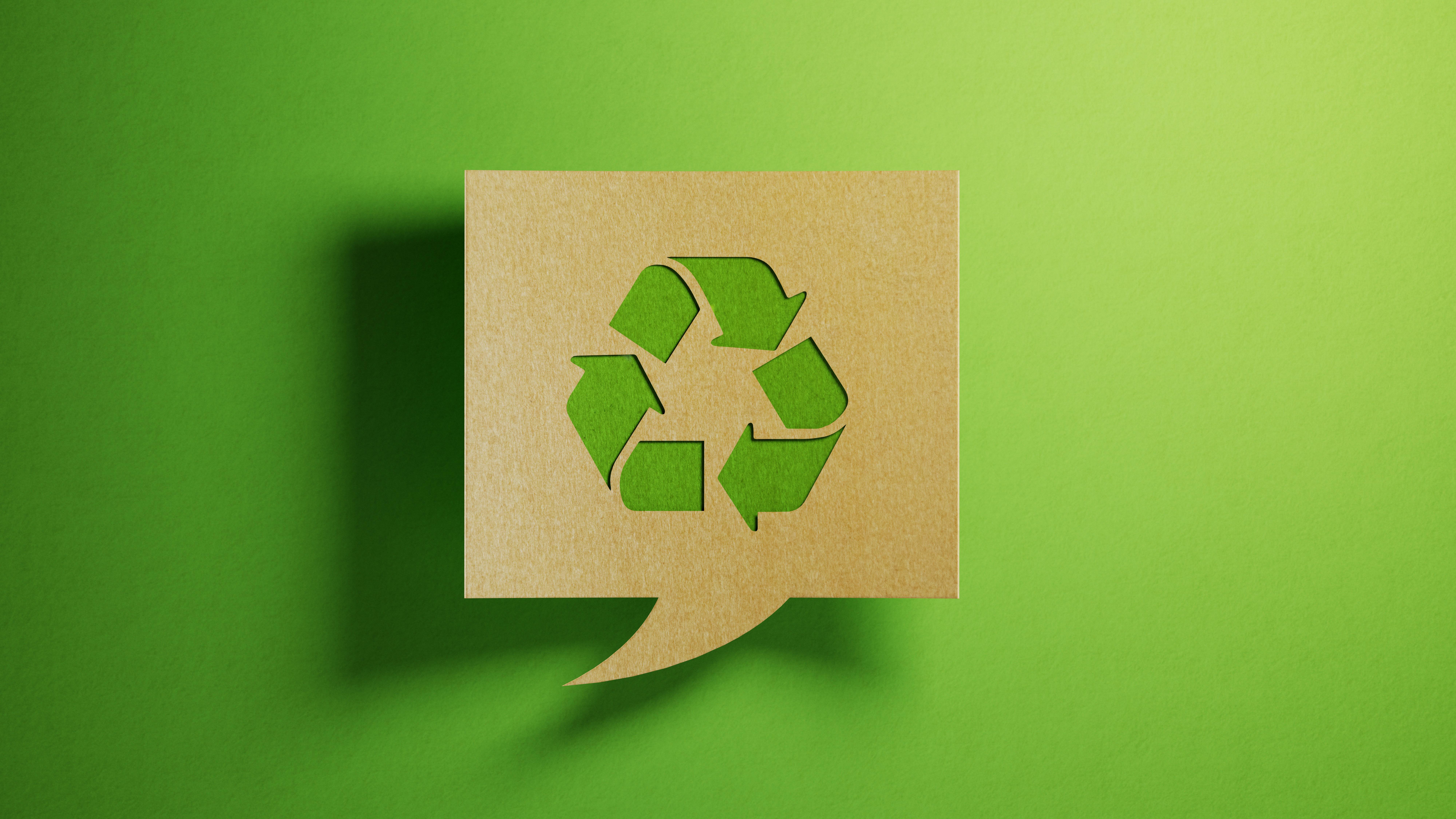A recycle symbol on a cardboard cutout speech bubble over a green background.