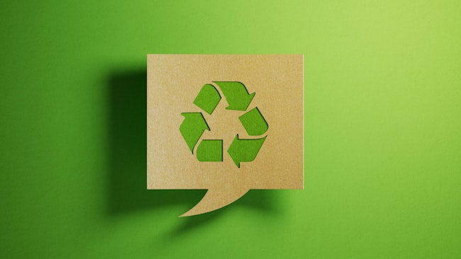 A recycle symbol on a cardboard cutout speech bubble over a green background.