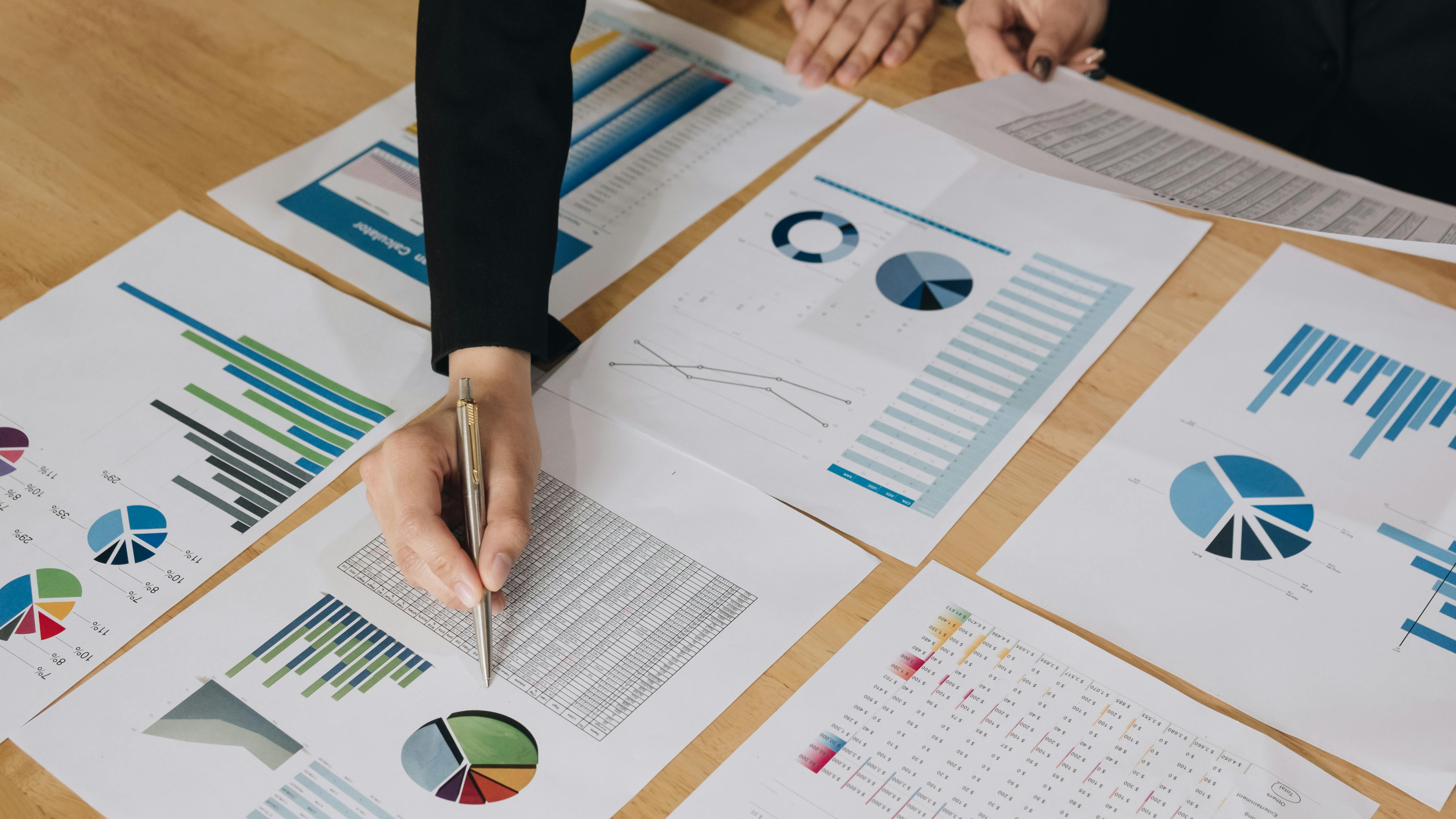 Businesspeople holding pens over graph paper.
