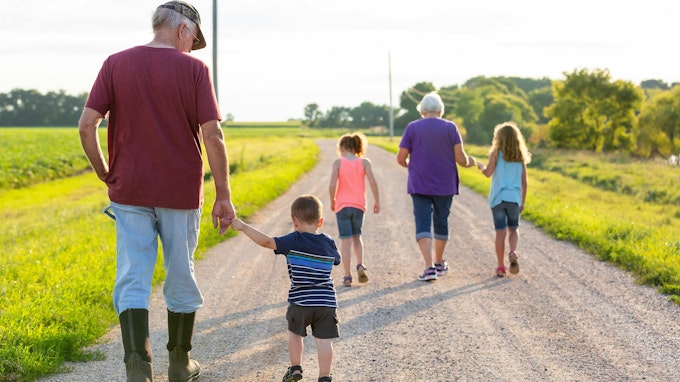 Three children walking with their grandparents down a rural gravel road.