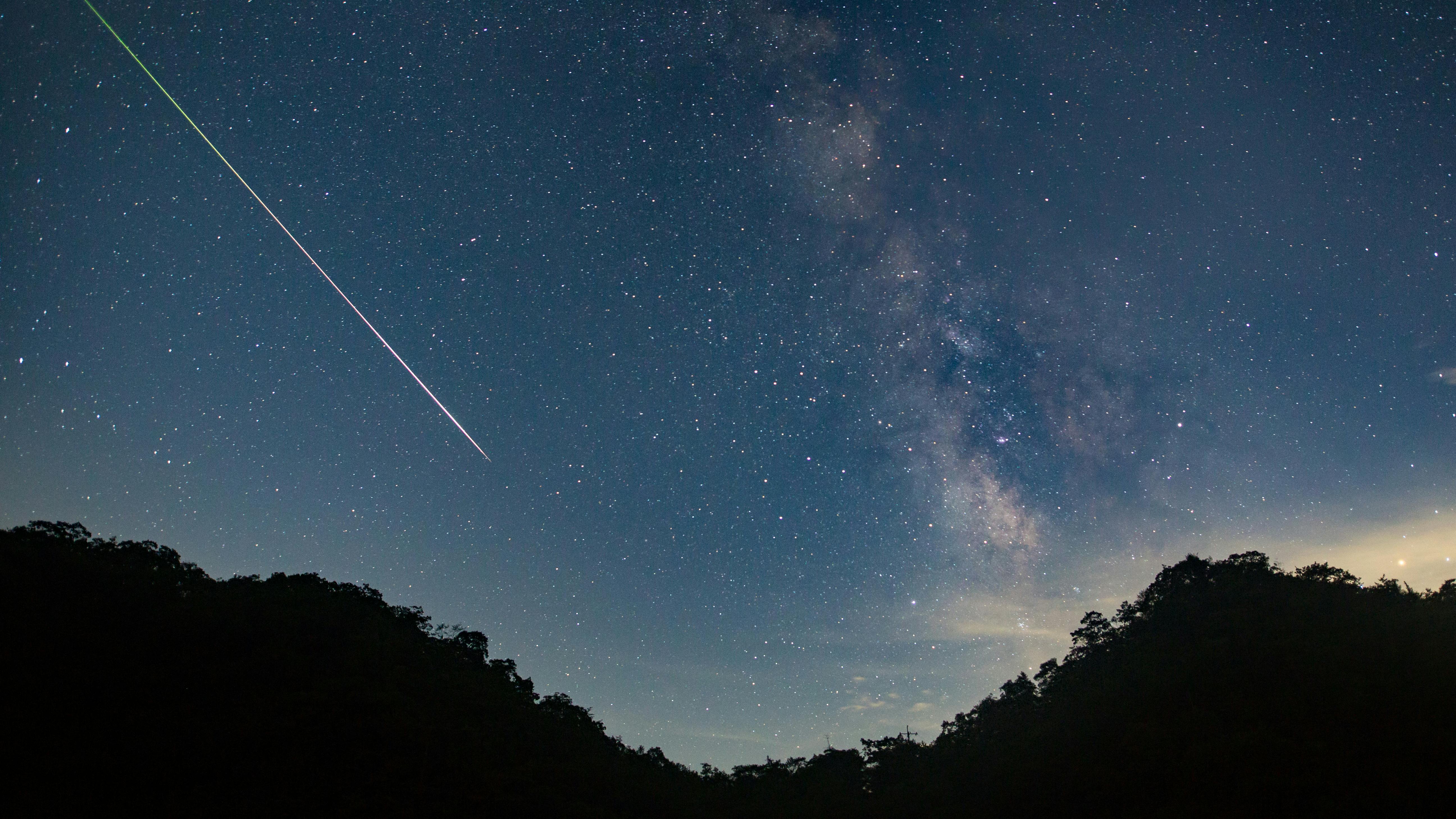 A meteor shoots across the night sky sky leaving a trail of light across the milky way